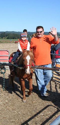 Photo of parent with child riding ponies at a pumpkin patch Fall Halloween fair.